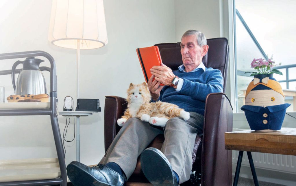Man in een stoel die in een oranje notebook kijkt met een pluche kat op schoot