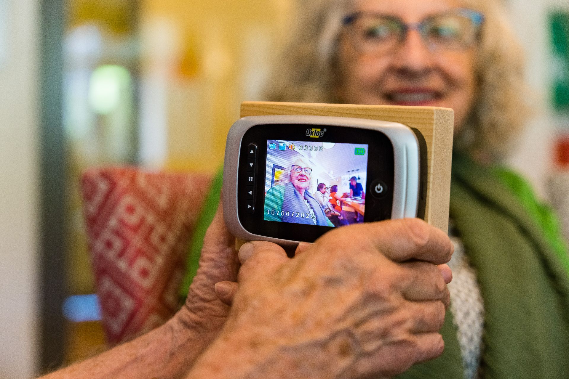 Twee handen die een slimme deurbel vasthouden met camera gericht op een vrouw in een ruimte