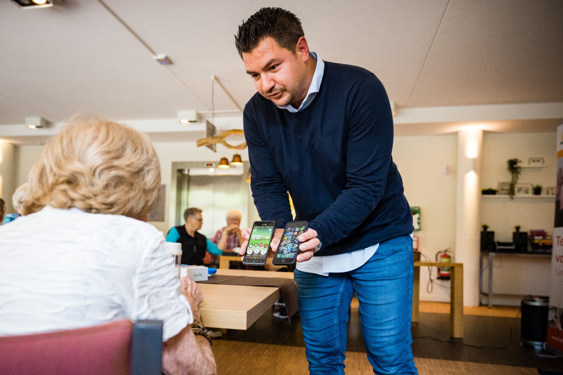 Man staat in een ruimte voor een vrouw met in elke hand een mobiele telefoon