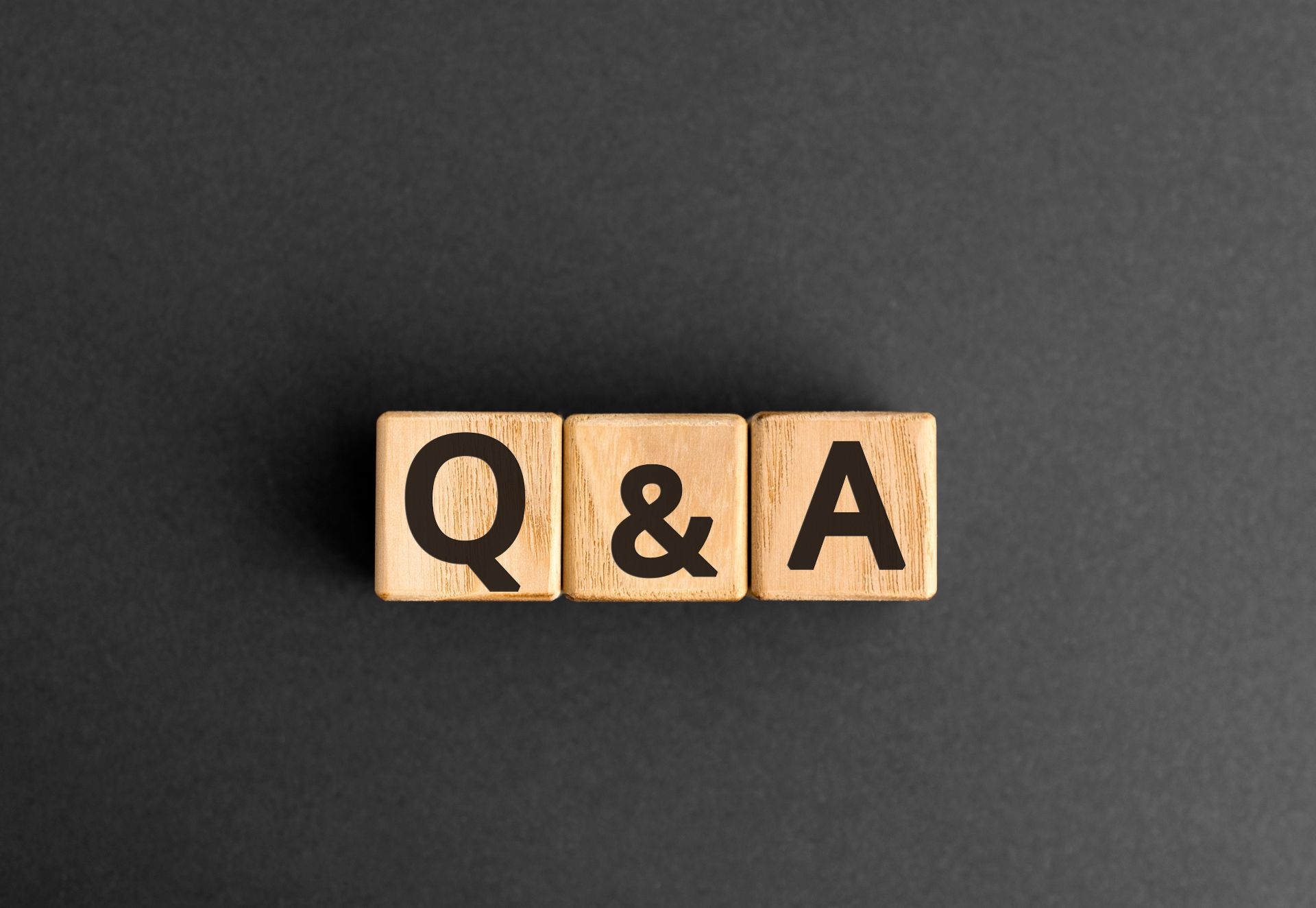 Drie houten blokjes naast elkaar met de letters Q & A op een zwarte achtergrond