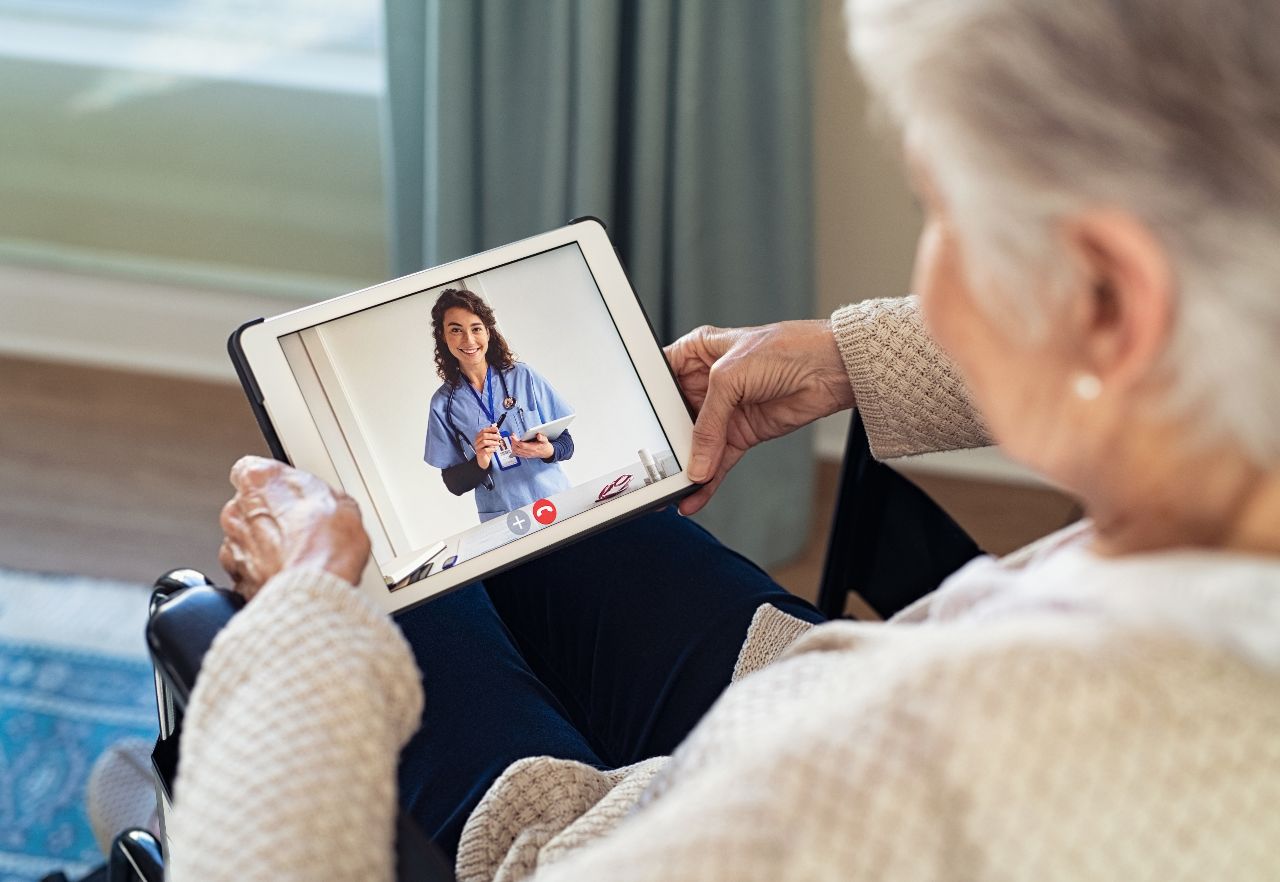 Vrouw in rolstoel communiceert via tablet met zorgprofessional via beeldbellen