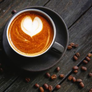 Een afbeelding van een kop koffie met in de schuimlaag een hartje en om het kopje heen liggen koffiebonen