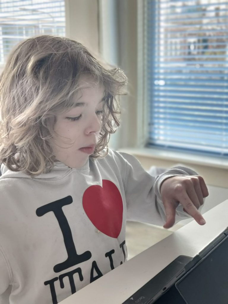 Een 12-jarig kind met donkerblonde krullen die op een tablet tikt